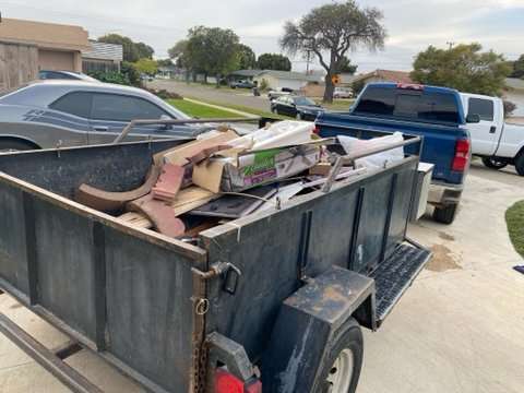 Open utility trailer loaded with broken wood, cardboard boxes and scrap on a residential street