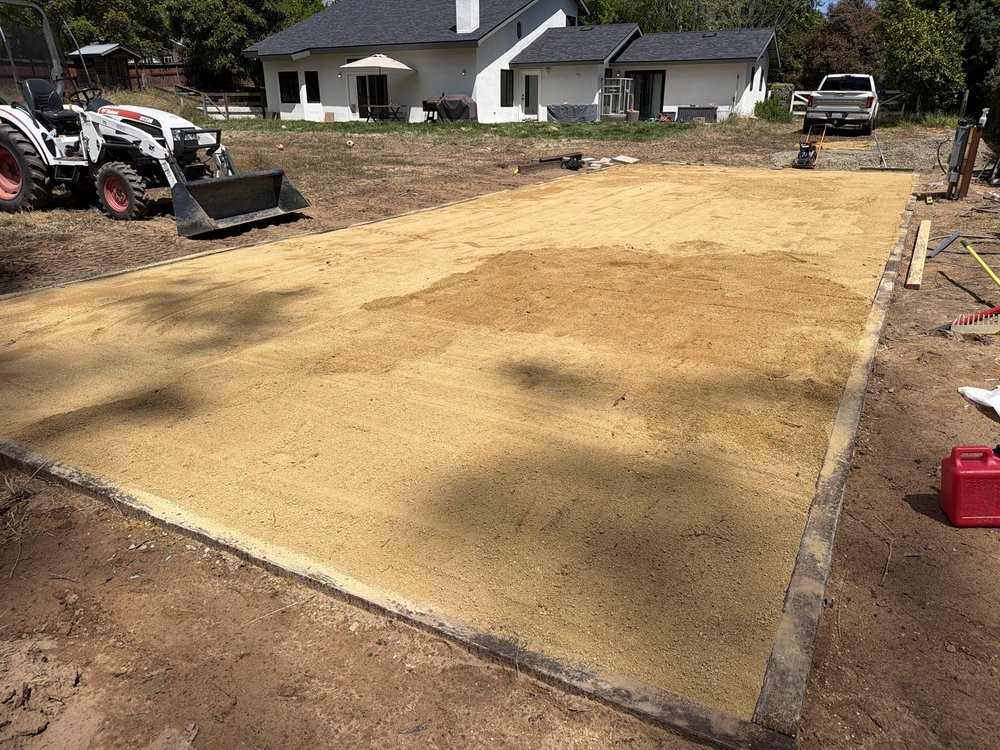 Rectangle of decomposed granite spread and edged with boards in a backyard, compact tractor parked beside it